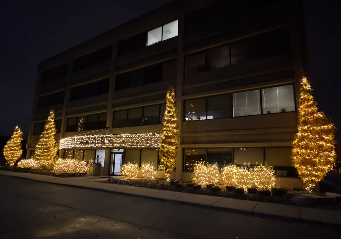 Commercial building frontage with wrapped trees and lit shrubs for the holidays