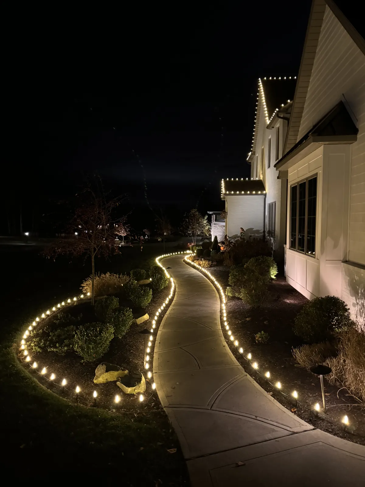 S-curve concrete walkway outlined on both sides with warm white C9 Christmas lights, leading to a home with a matching lit roofline